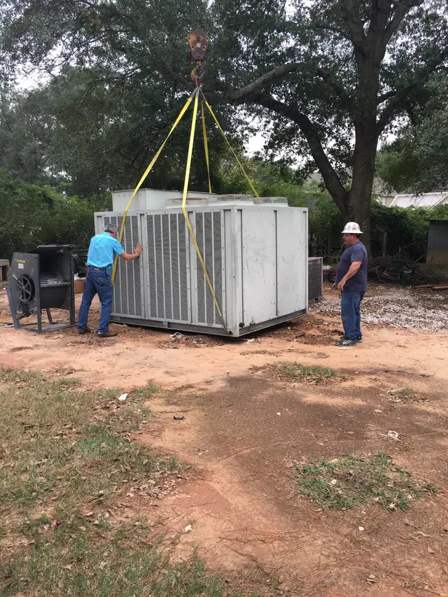 A crane lifts a large commercial package HVAC unit on slings while two Champion and Nash technicians guide it into place on a rooftop